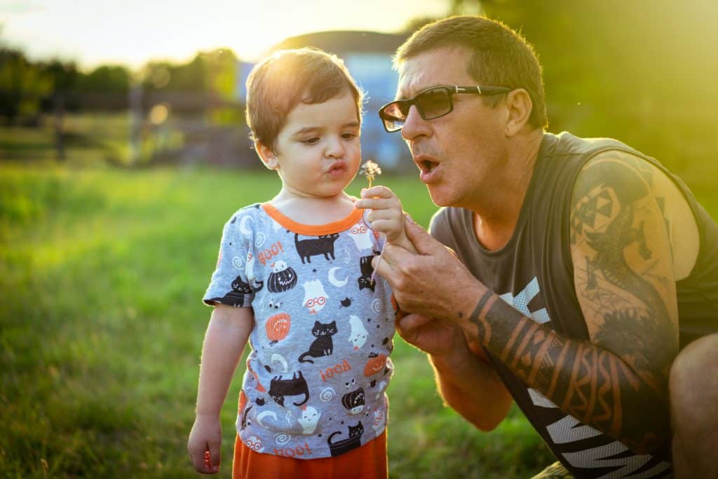 Adulto com braço tatuado brincando com criança no sol